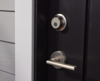 Satin nickel door handle and lock on black door with white molding and grey siding.