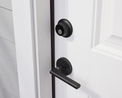 Matte black door handle and deadbolt on white door with white trim and light grey siding.