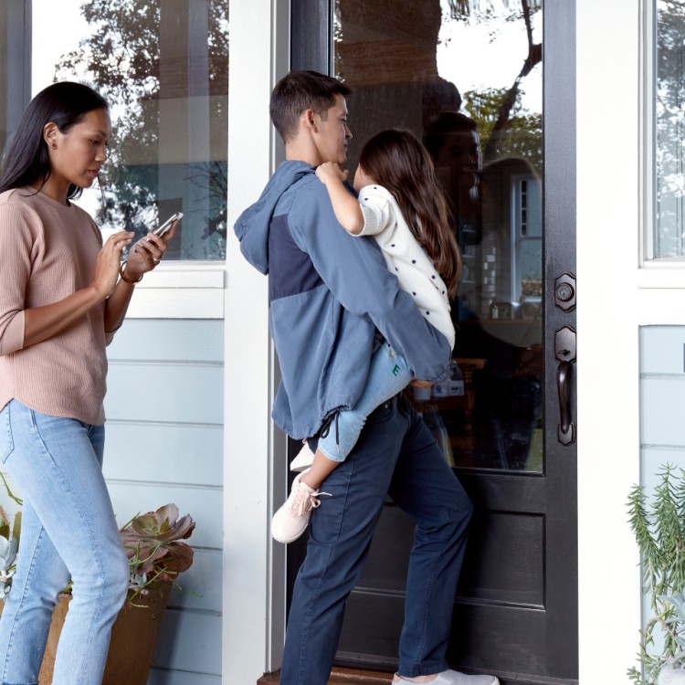 Mother and father carrying young daughter, approaching front door front the outside, with a Level lock installed in the door.